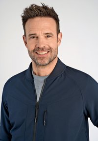 Granatowa kurtka zapinana na zamek z wysokim kołnierzem, z szarym wewnętrznym materiałem i dwiema kieszeniami zapinanymi na zamek. Gładka tkanina i wyraźne szwy.