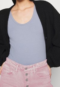 Cárdigan negro de canalé sobre una camiseta sin mangas de canalé azul claro, combinado con una falda de mezclilla rosa de tiro alto con botones frontales y bolsillos.