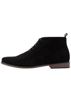 Bottine en daim noir avec fermeture à lacets à l'avant, bout rond, languette au talon et semelle à talon bas marron.