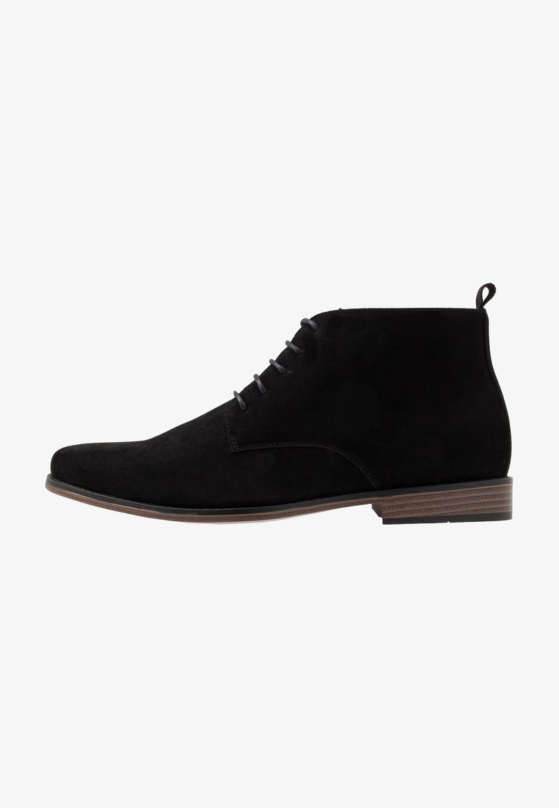 Bottine en daim noir avec fermeture à lacets à l'avant, bout rond, languette au talon et semelle à talon bas marron.