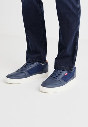 Navy blue sneakers made of leather and mesh with white rubber soles. Features lace-up front and a small red brand logo on the side.