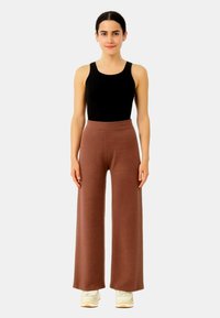 Pantaloni larghi marroni realizzati in un morbido tessuto a maglia, con vita alta. Abbinati a una canotta nera e a sneaker di colore chiaro.
