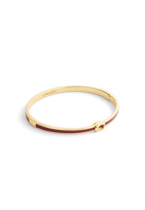 Guldfarvet bangle-armbånd med en maroon indlægning, glat overflade og en cirkulær lås med mærkenavnet "COACH" indgraveret indeni.