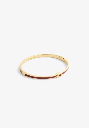Bracelet jonc en ton or avec une incrustation maroon, texture lisse et un fermoir circulaire avec le nom de la marque "COACH" gravé à l'intérieur.