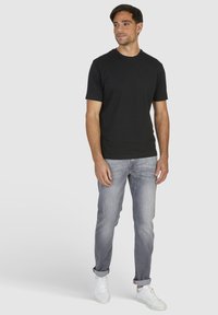 T-shirt noir à col rond en coton, porté avec un jean gris clair et des baskets blanches. Coupe décontractée avec des manches courtes et un design simple.