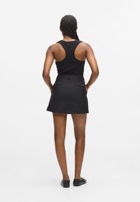 Čierny bezrukávový top v kombinácii s čiernou mini sukňou, ktorá má priliehavý strih a dve zadné vrecká. Hladká látka s čistým zakončením.