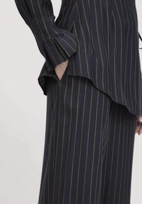 Outfit a righe navy composto da una blusa morbida con orlo asimmetrico e pantaloni a gamba larga. Le righe gialle aggiungono contrasto. Il tessuto sembra testurizzato.