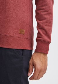 Bordeaux pullover sweatshirt met ribgebreide manchetten en onderkant, met een gestructureerde stof en een bruine leren label aan de linksonder.