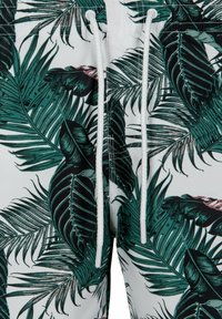 Shorts de bain en tissu léger avec un motif de feuilles tropicales vertes et noires sur fond blanc. Comprend un cordon de serrage blanc.