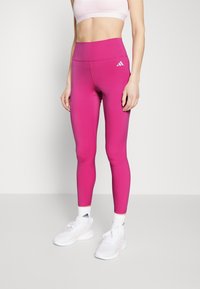Dopasowane różowe legginsy wykonane z elastycznego materiału, z wysokim stanem i małym białym logo Adidas z boku.