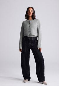 Szürke rövidített kardigán kerek nyakkivágással és gombos záródással, magas derekú fekete, bőszárú farmerral és mintás slip-on cipővel párosítva.