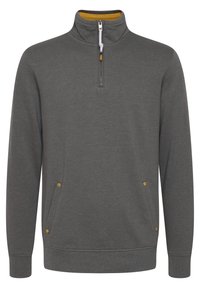 Sudadera gris de cuello alto, con medio cierre, dos bolsillos laterales y acentos amarillos en el cierre y los bolsillos. Textura suave.