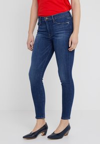 Jeans ajustados de mezclilla azul con cintura de altura media, bolsillos delanteros y una textura suave. Combinados con unos tacones de charol azul marino.