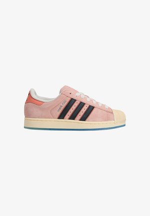 Różowy zamszowy sneaker z czarnymi paskami, gumowym noskiem i kremową podeszwą środkową. Posiada białe sznurowanie i kontrastową zakładkę na pięcie.