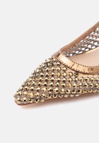 Tippkärjega lahtises kingas kuldse metallilise äärise ja võrgust pealiskihiga, mis on kaunistatud läikivate kuldsete ja hõbedaste rhinestone'idega.