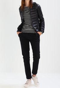 Doudoune matelassée noire, chemise à rayures à manches longues, pantalon noir et baskets blanches. Comprend des poches zippées et une capuche.