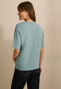 Maglietta azzurra a maniche corte con vestibilità morbida e scollo rotondo, realizzata in un tessuto morbido. La vista posteriore mostra una texture liscia e un design semplice.