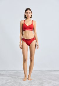 Rød undertøysett med en v-hals bralette og matchende bikinitruse, med myk stoff og kontrasterende svarte elastiske bånd med merke.