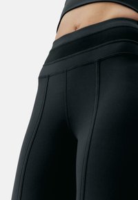Fekete magas derekú leggings lapos varrással, sima matt felülettel és testhezálló kialakítással, amely a derektól a comb közepéig terjed.