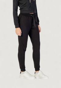 Czarne, tapered spodnie dresowe wykonane z miękkiego materiału, z elastycznym paskiem w talii na sznurek oraz ribbowymi mankietami na kostkach.