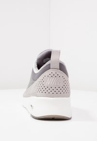 Grå Nike-sneaker med en strömlinjeformad design, en överdel av mocka och mesh, vadderad krage och perforerade detaljer på hälen.