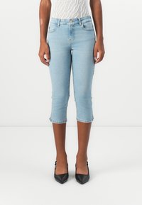 Light blue cropped jeans with a high waist, featuring a fitted design, frayed hem, and classic five-pocket styling. Worn with black heels.