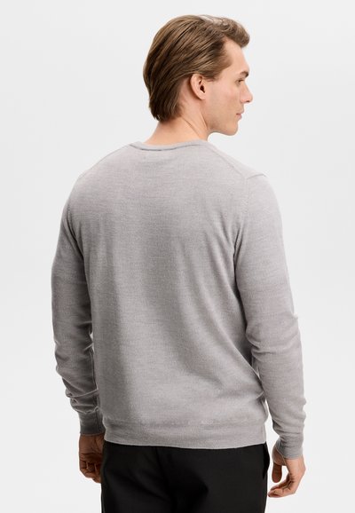 Άνδρας που φοράει ανοιχτό γκρι πουλόβερ με μακριά μανίκια και μαύρο παντελόνι, φαίνεται από την πίσω πλευρά και κοιτάζει προς τα δεξιά του.