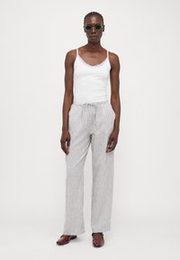 Camisola bianca con pizzo, abbinata a pantaloni a palazzo a righe chiare. Il modello indossa occhiali da sole rotondi e scarpe basse rosse. Design semplice.