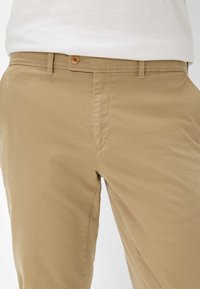 Khakifarbene Baumwollhosen verfügen über einen Knopfverschluss, leichtes Steppnähte und eine glatte Textur. Seitentaschen sichtbar; Standard-Fit-Design.