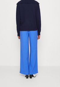 Blue wide-leg trousers paired with a navy knit sweater featuring a large collar. The fabric appears soft with a smooth texture.
