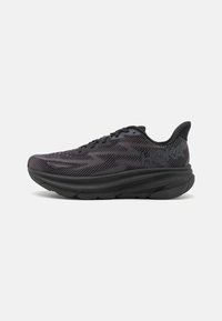 Scarpa sportiva nera con upper in mesh, motivo testurizzato, suola rialzata e logo del marchio in evidenza. Presenta una punta arrotondata e suola flessibile.