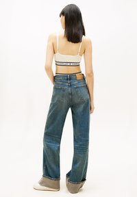 Pantalones vaqueros de pierna ancha en azul desvaído, con cintura alta y un parche de cuero marrón contrastante en la parte trasera, con un ajuste holgado.