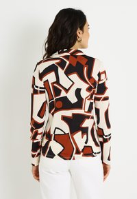 Top de manga larga en un patrón abstracto multicolor que presenta tonos negros, blancos y óxido. Fabricado en una tela suave con un diseño ajustado.