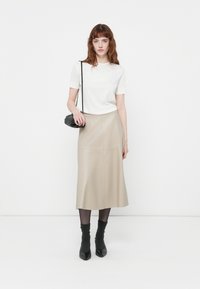 Beige nep leren midi-rok met een uitlopende vorm, gecombineerd met een witte top met korte mouwen en zwarte gestructureerde enkellaarzen.