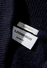 Ciemnogranata tkanina z jagnięcej wełny z metką zawierającą dwie etykiety: jedna z napisem "LINDENBERGH" pogrubioną czcionką, druga z napisem "RELAXED FIT" i "LAMBS WOOL" mniejszym tekstem.