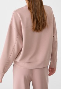 Helles rosa Sweatshirt mit lässiger Passform, gerippten Bündchen und Saum. Hat eine glatte Textur und einfache Nahtdetails auf der Rückseite.