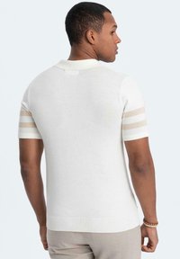 Kortärmad vit stickad polo med horisontella beige ränder på ärmarna, ribbat krage och nederkant, med en mjuk textur och figurnära passform.