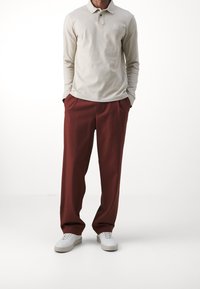 Lichtbeige polo met lange mouwen en een kraag, gecombineerd met losse, donkerrode broeken en witte sneakers. Eenvoudig ontwerp, geen zichtbare patronen.
