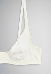 White soft fabric bra with thin adjustable straps and delicate trim along the edges, shown against a gray background.
