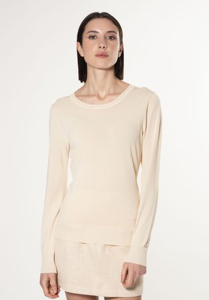 Maglione beige a maniche lunghe con design aderente, scollo rotondo, e polsini e orlo a costine. Texture liscia, dettaglio hardware minimale.