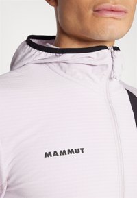 Ανοιχτό μωβ επώνυμο μπουφάν με ψηλό γιακά, μπροστινό φερμουάρ και μαύρες λεπτομέρειες. Υφασμα με υφή και διακριτό σχέδιο.