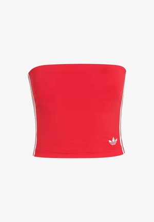 Červený crop top bez ramienok vyrobený z elastického materiálu s bielymi bočnými pruhmi a bielym logom v dolnom ľavom rohu. Hladká textúra.