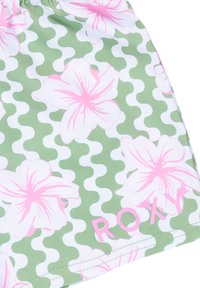 Gröna badshorts med ett vitt och rosa blommönster, vågigt mönster och "ROXY" tryckt i rosa vid fållen.