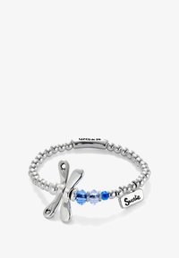 La pulsera de cuentas plateadas presenta un charm de libélula, cuentas de cristal azul y una etiqueta grabada que dice "Suerte". Textura metálica suave y acabado pulido.