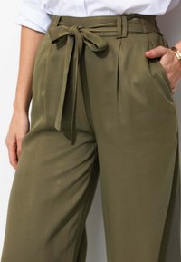 Pantalons vert olive taille haute avec une coupe large, dotés de plis et d'une ceinture à nouer, fabriqués à partir d'un tissu lisse et léger.