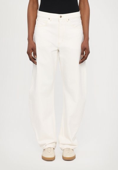 Jean large blanc en denim, avec cinq poches, un bouton et une fermeture éclair, et des détails de couture beiges.