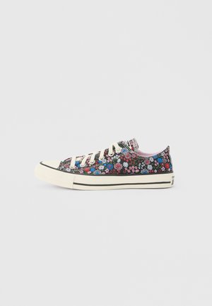 Lage canvas sneaker met witte zool en veters, met een kleurrijke bloemenprint op een zwarte achtergrond.