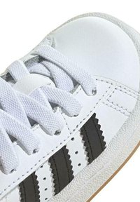 Weiße Sneaker mit glattem Lederobermaterial, strukturiertem Gummisohle, Baumwollsenkeln und drei schwarzen gezackten Streifen an der Seite.
