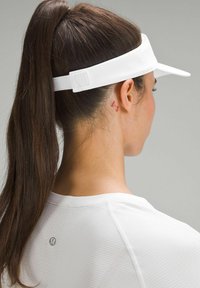 Bílý kšilt s texturovanou látkou, nastavitelným páskem vzadu a elegantním designem. Nošený s lehkým bílým sportovním topem.