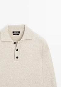 Jasnobeżowy wełniany sweter z fakturowanym splotem, prążkowanym kołnierzem i trzema czarnymi guzikami przy rozcięciu dla zamknięcia.